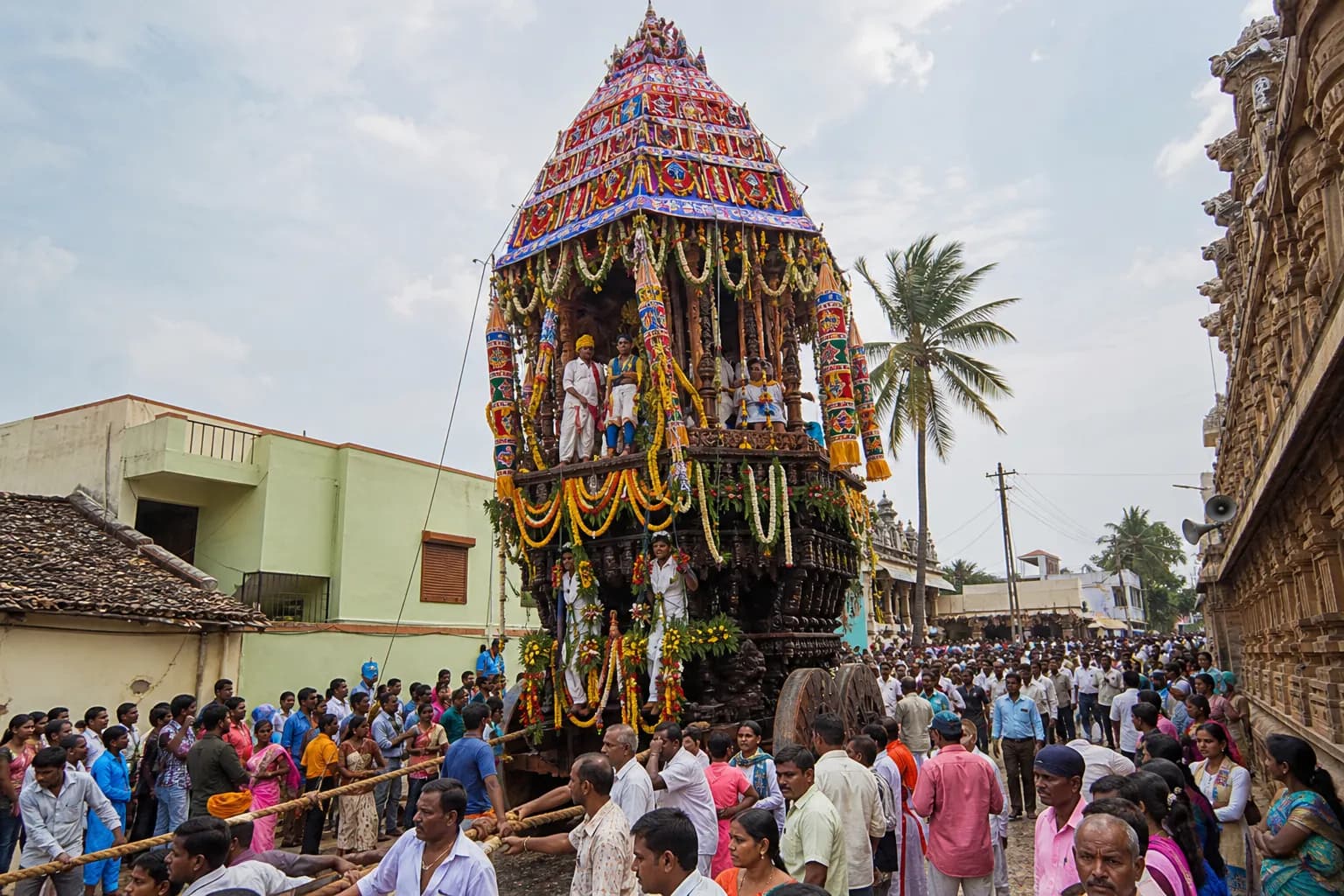 A decorated wooden temple chariot surrounded by a crowd at a Karnataka rathotsava